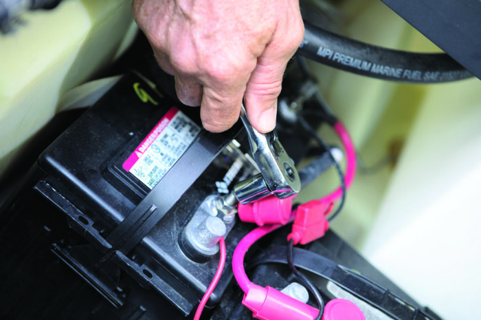 Hand using a wrench on a battery terminal.